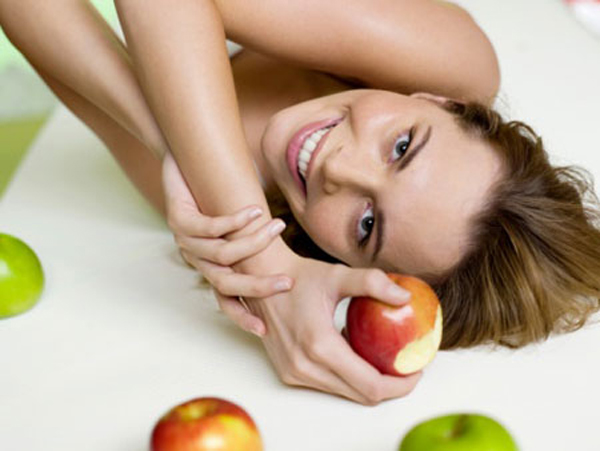 Woman lying on bed with apples, smiling