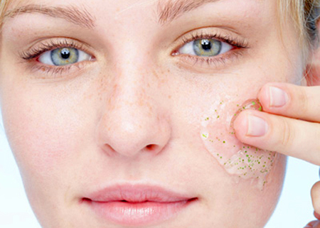Young woman applying exfoliating gel to face, portrait, close-up